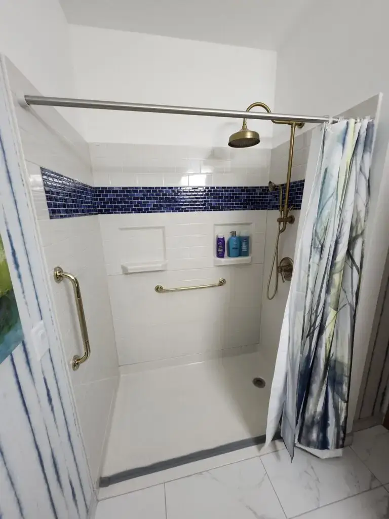 Photograph of a shower remodel with grab bars, custom blue tile, zero entry shower, and a shower head with handheld nozzle system completed by Adaptive Remodeling Solutions
