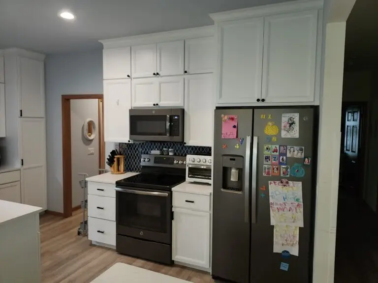 Photograph of a kitchen remodel completed by Adaptive Remodeling Solutions. The remodel features a large fridge, white kitchen cabinets, a microwave, and oven.
