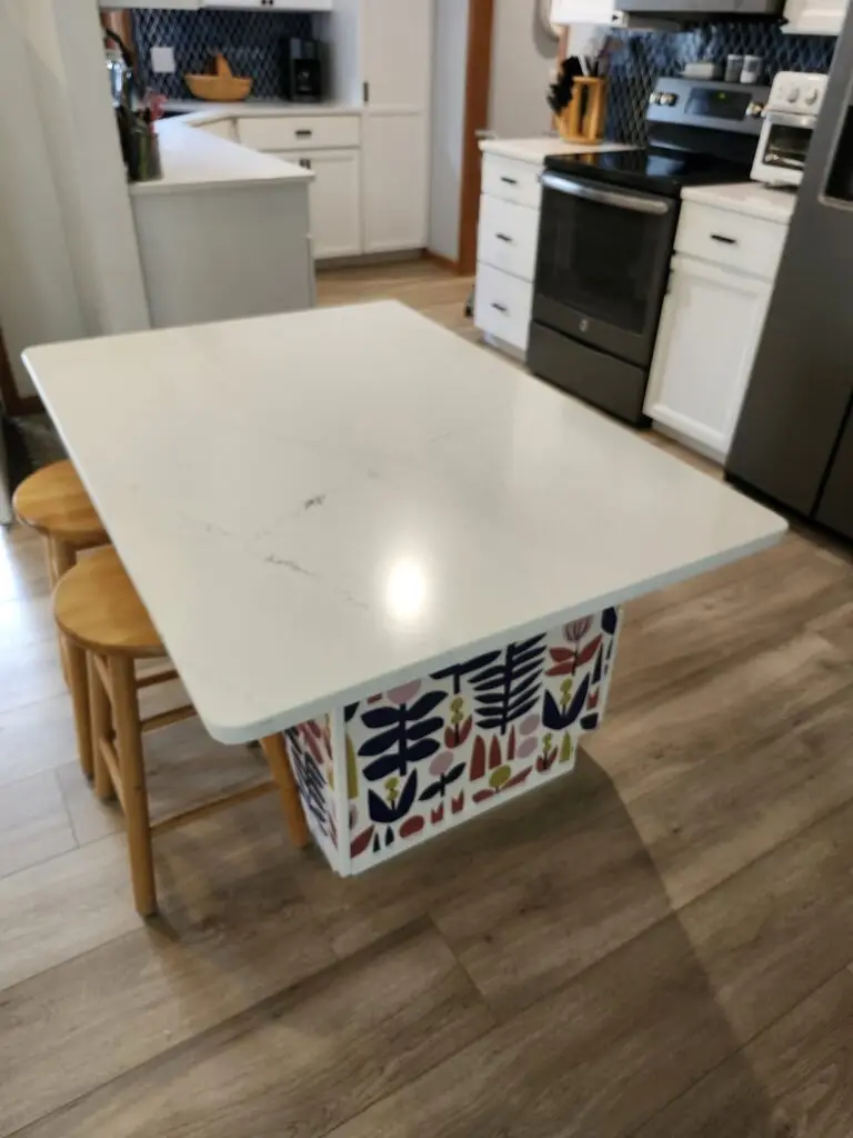 Photograph of an island with two wooden bar stools in the center of a kitchen. The island leaves enough space for a wheelchair to enter below. Installation completed by Adaptive Remodeling Solutions.