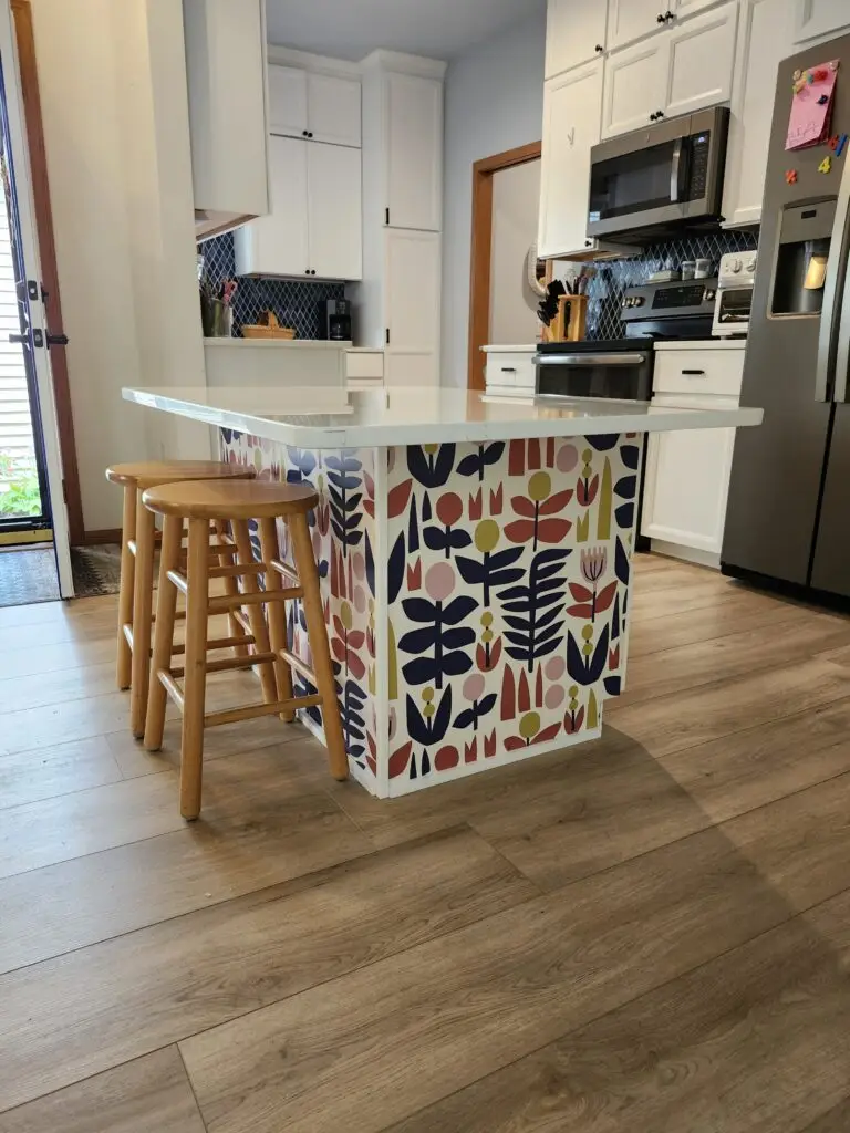 Photograph of an island with two wooden bar stools in the center of a kitchen. The island leaves enough space for a wheelchair to enter below. Installation completed by Adaptive Remodeling Solutions.