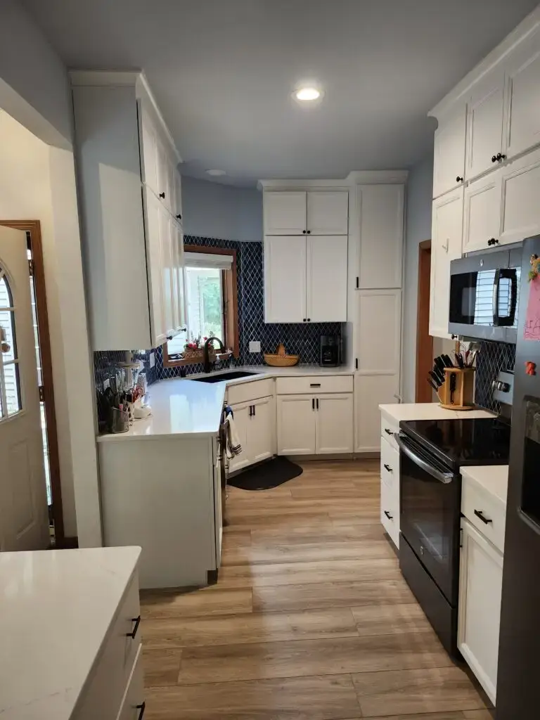 Photograph of a kitchen remodel completed by Adaptive Remodeling Solutions. The remodel features a large fridge, white kitchen cabinets, kitchen counter with corner sink, a microwave, and oven.