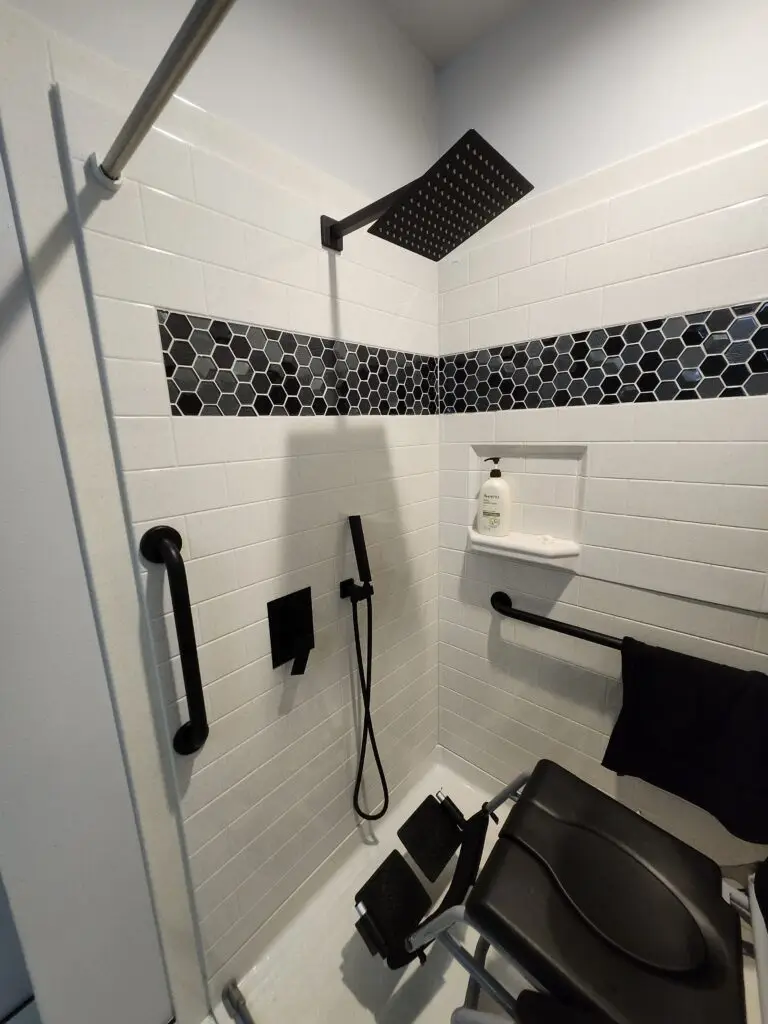 Photograph of a modern shower remodel completed by Adaptive Remodeling Solutions, featuring custom tile, a detachable nozzle, large flat rain shower head, and grab bars.
