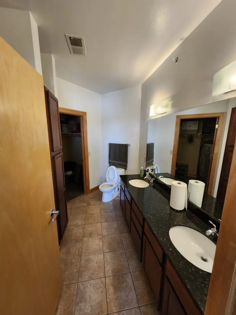 Photograph of a bathroom remodel by Adaptive Remodeling Solutions, depicting dual sinks, large mirror, and a toilet.