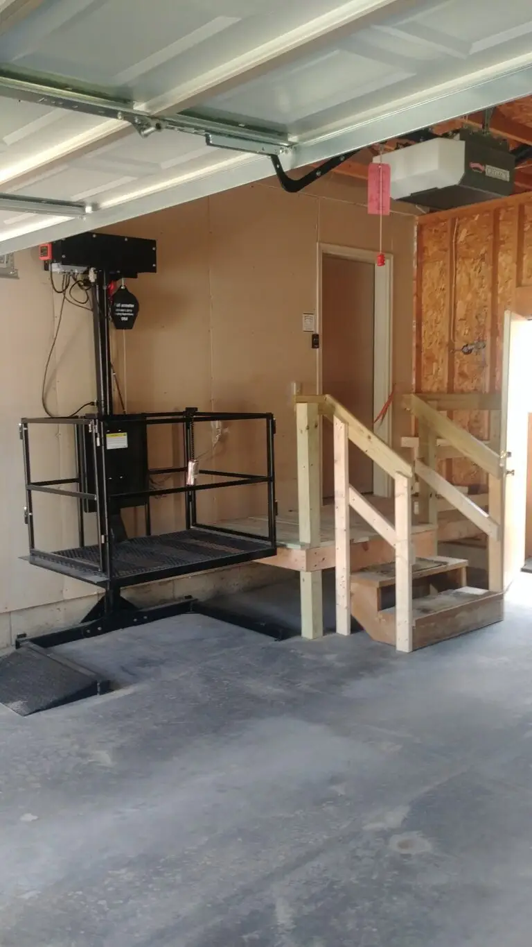 Photograph of a wheelchair lift next to a set of wooden stairs inside a garage, installed by Adaptive Remodeling Solutions.