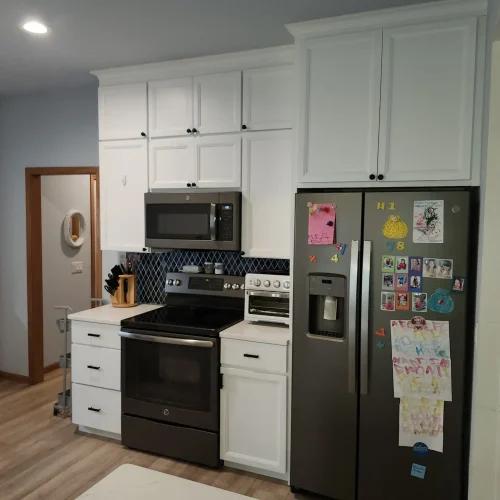 Photograph of a kitchen remodel completed by Adaptive Remodeling Solutions. The remodel features a large fridge, white kitchen cabinets, a microwave, and oven.