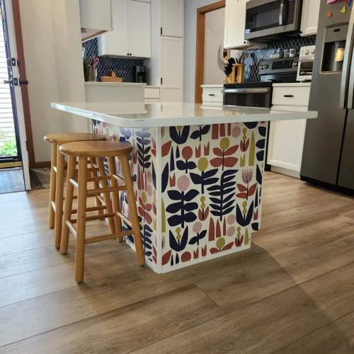 Photograph of an island with two wooden bar stools in the center of a kitchen. The island leaves enough space for a wheelchair to enter below. Installation completed by Adaptive Remodeling Solutions.