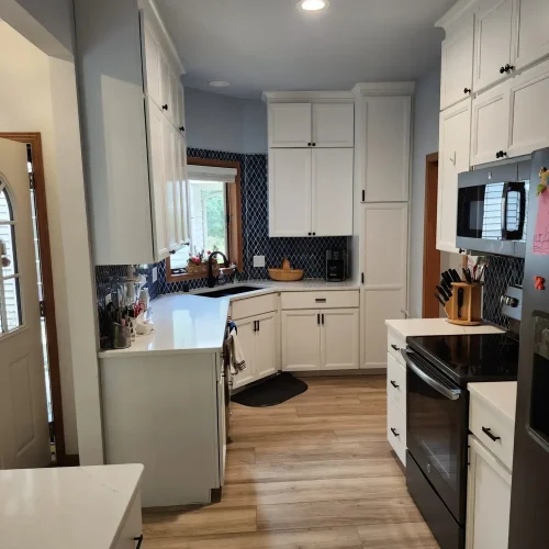 Photograph of a kitchen remodel completed by Adaptive Remodeling Solutions. The remodel features a large fridge, white kitchen cabinets, kitchen counter with corner sink, a microwave, and oven.