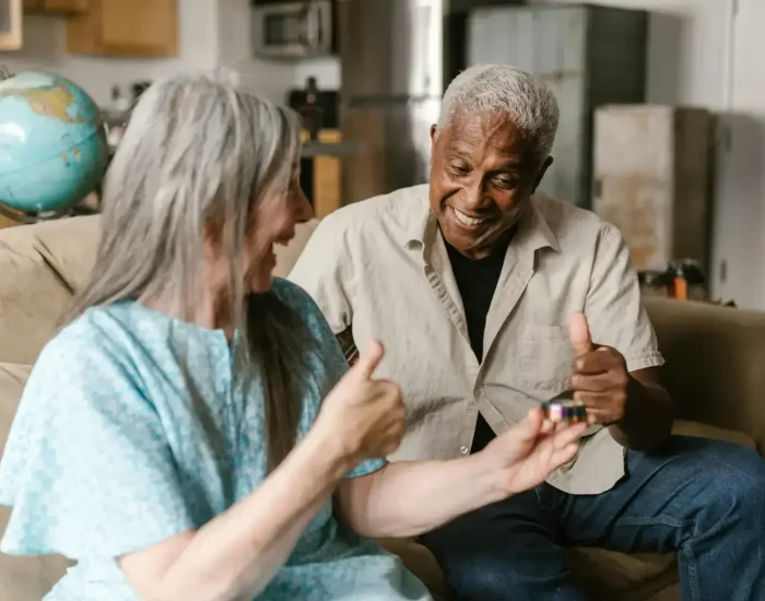 A senior man and senior woman laughing together in a kitchen and living room setting.